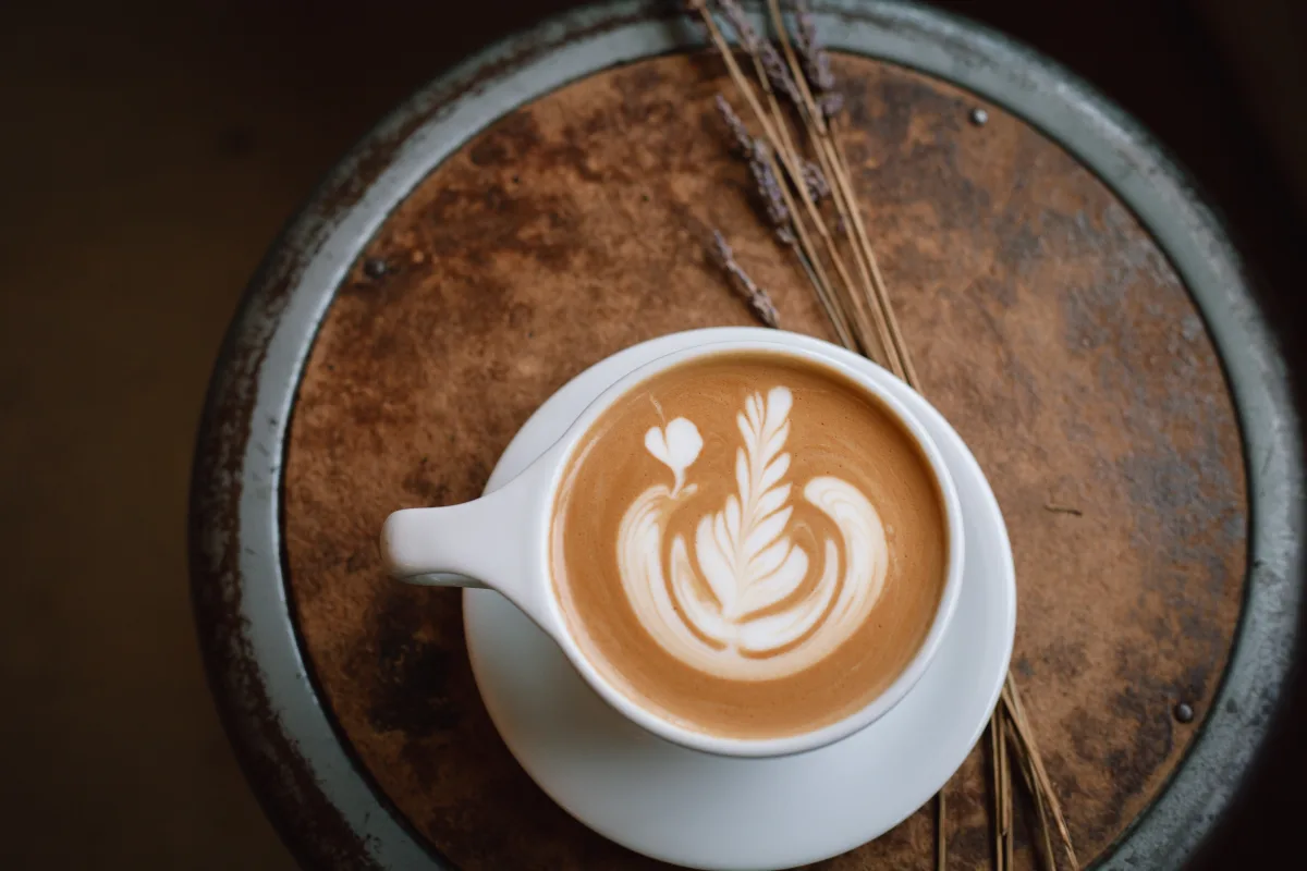 Latte with rosetta milk art in a white cup on a rustic wood table at Adesso